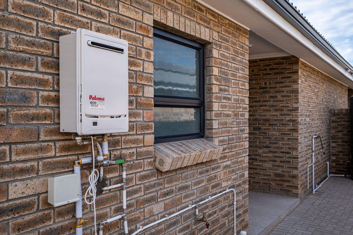 Exterior view of a townhouse featuring a wall-mounted Paloma gas water heater, brick facade, and external plumbing fixtures.