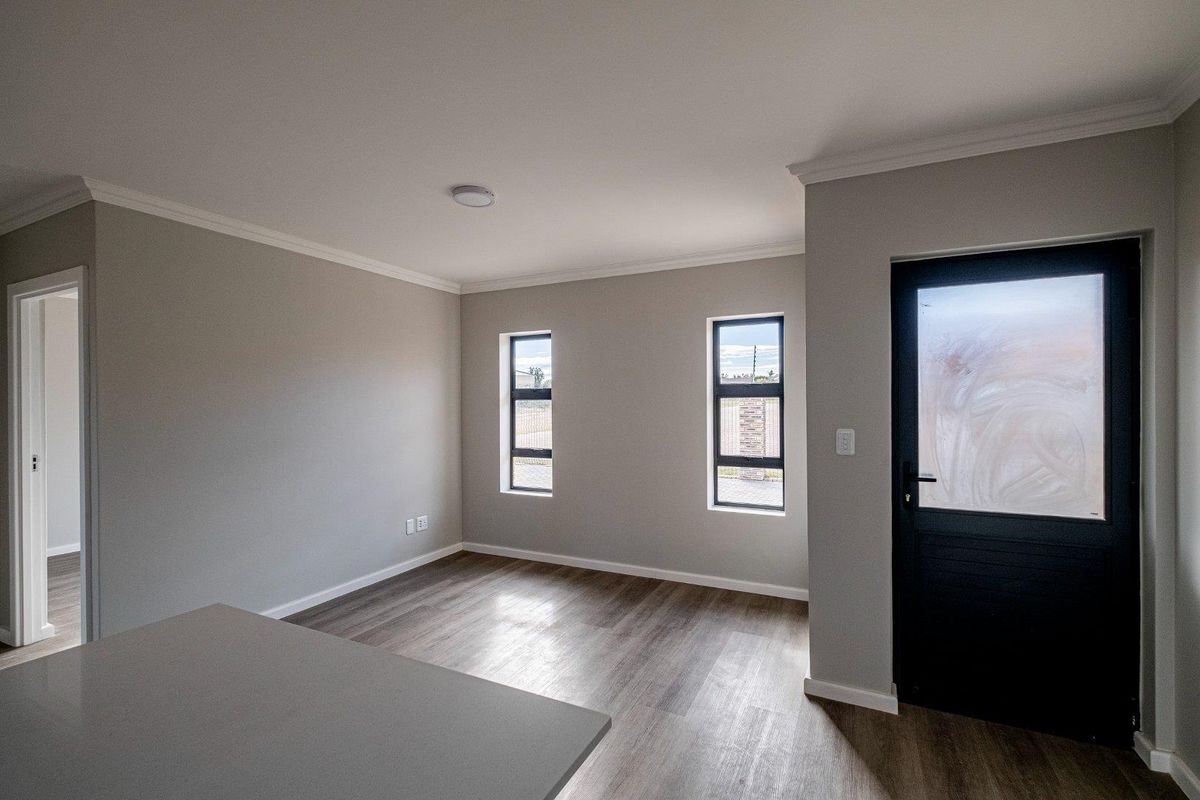 A bright, modern, and empty living area featuring neutral walls, wood-look flooring, and a dark-framed exterior door with frosted glass.