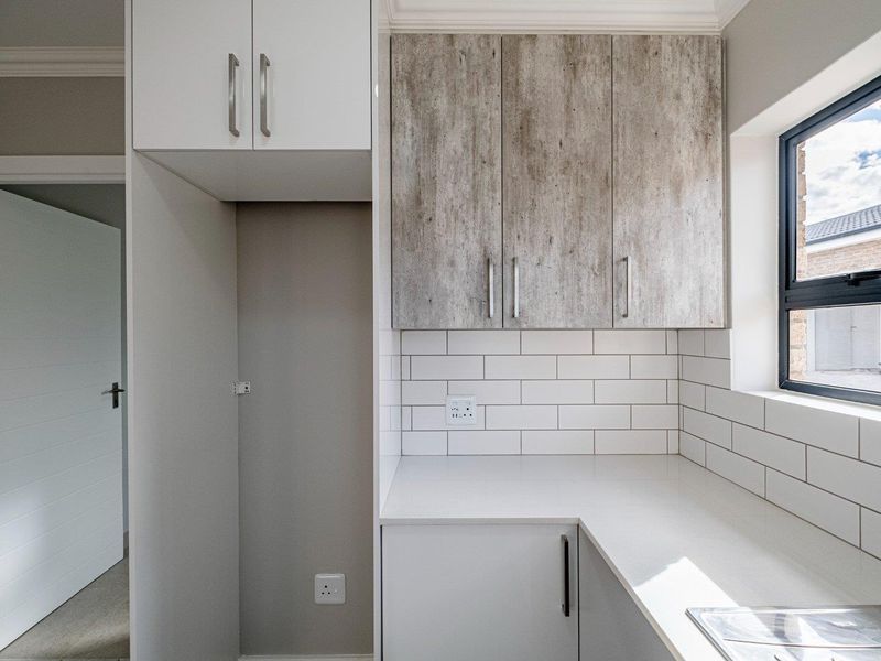 A clean and modern scullery featuring built-in cabinetry, subway tile backsplash, and quartz countertops with an integrated sink.