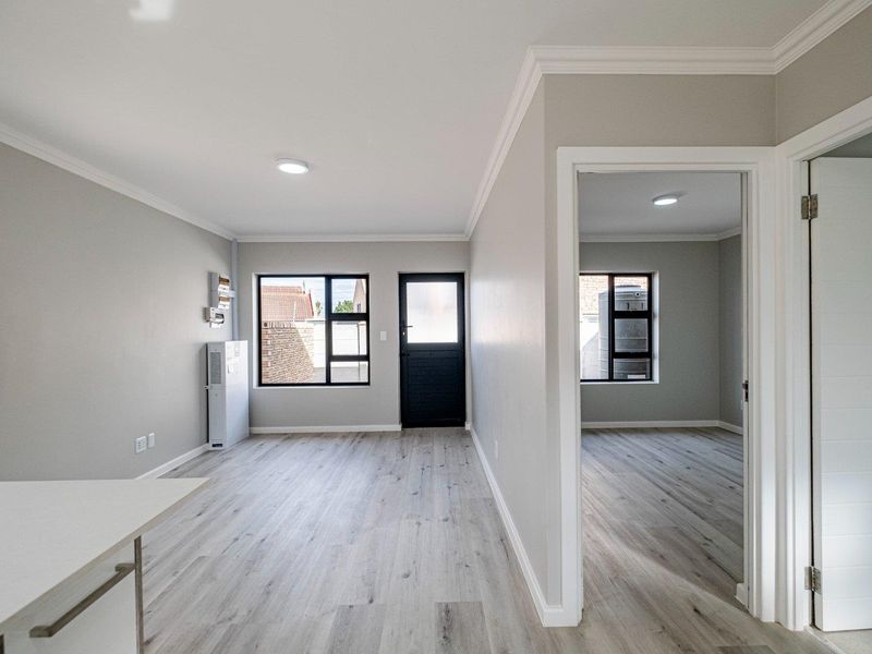 A bright, modern open-plan living area featuring light-toned laminate flooring, crisp neutral walls, recessed lighting, and clean architectural lines throughout the space.