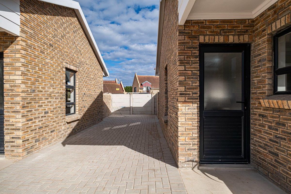 A clean, paved rear courtyard area between two face brick townhouse structures, featuring secure boundary walling and modern aluminium window frames.