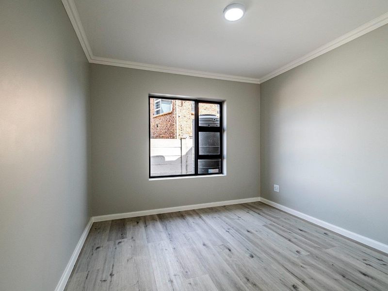 A clean, empty bedroom featuring modern light-toned laminate flooring, neutral grey walls, and a contemporary aluminium-framed window.