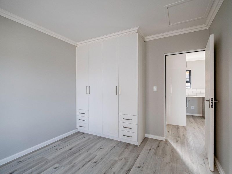 A bright, modern bedroom featuring neutral grey walls, light wood-look laminate flooring, and ample built-in cupboard storage with a clean, contemporary finish.