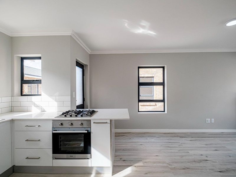 Modern open-plan kitchen and living area featuring light laminate flooring, sleek white cabinetry, gas hob, built-in oven, and contemporary subway tile backsplash.