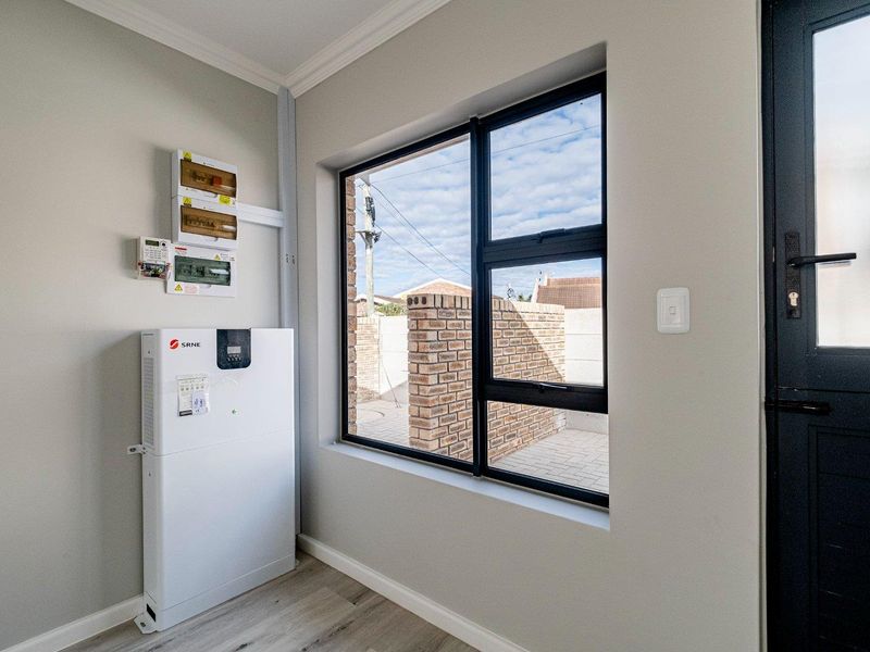 A clean utility space featuring a modern solar inverter system, electrical distribution board, laminate flooring, and a large window overlooking the exterior area.