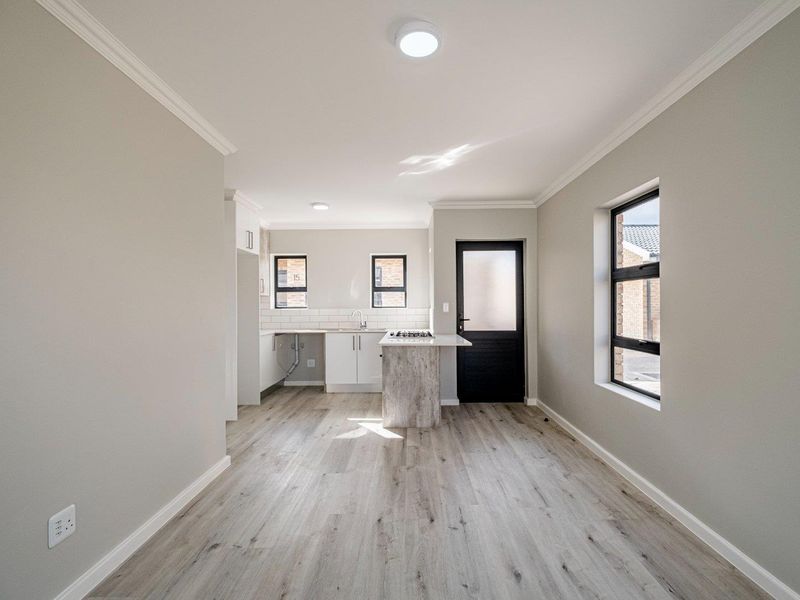 A bright, modern kitchen featuring clean white cabinetry, a gas hob, tiled backsplash, and durable laminate flooring with direct access to the exterior.