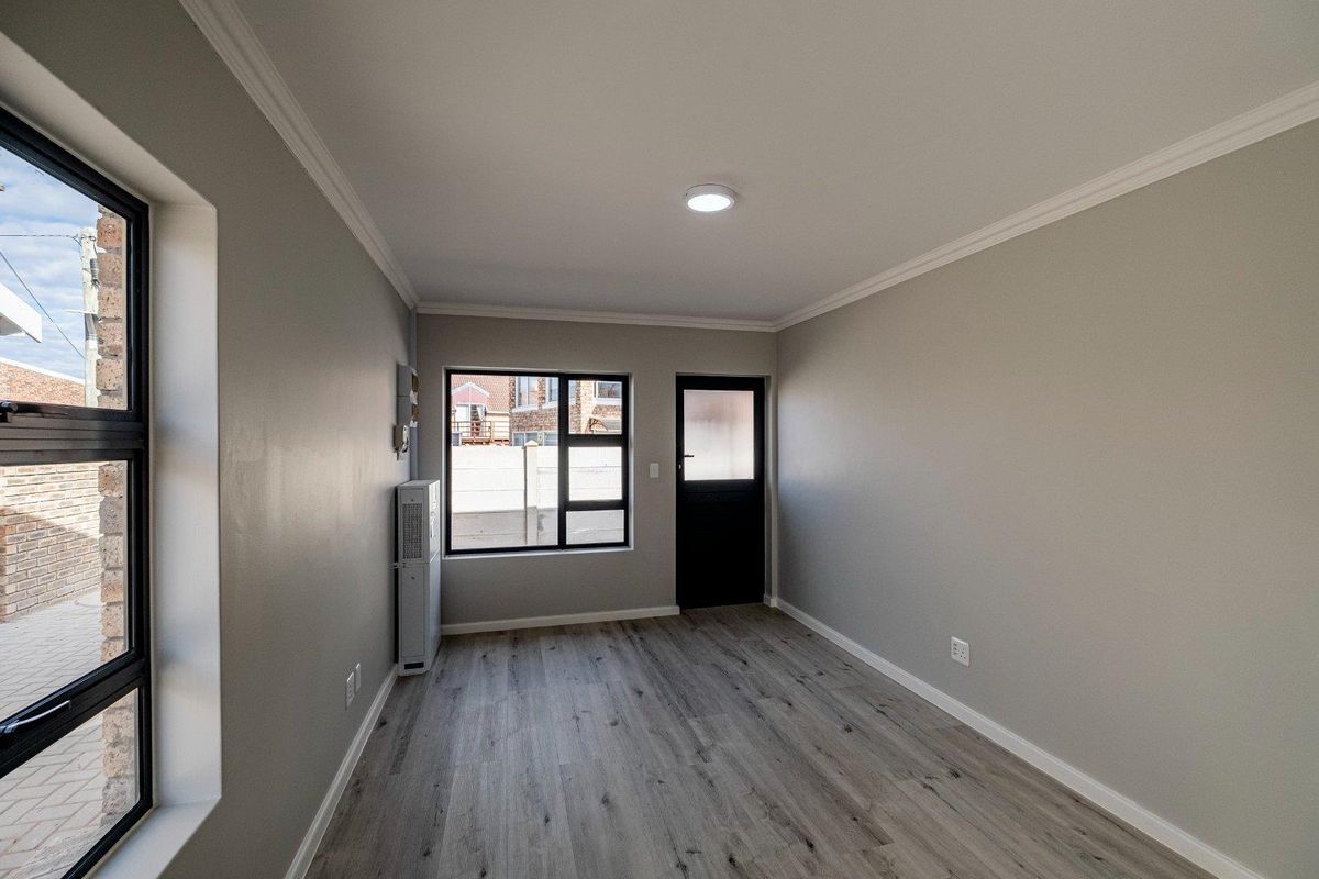 A clean, empty bedroom featuring modern laminate flooring, neutral grey walls, cornice detailing, and direct access to the exterior via a private door.