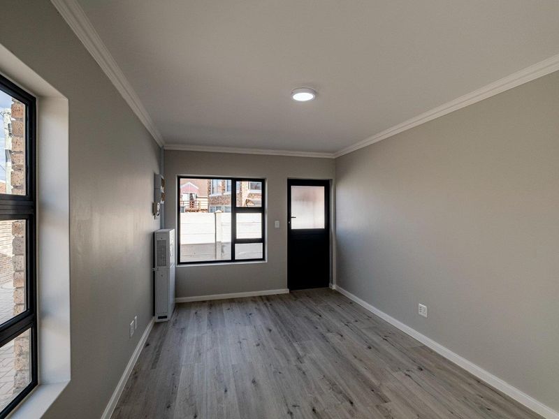 A clean, empty bedroom featuring modern laminate flooring, neutral grey walls, cornice detailing, and direct access to the exterior via a private door.