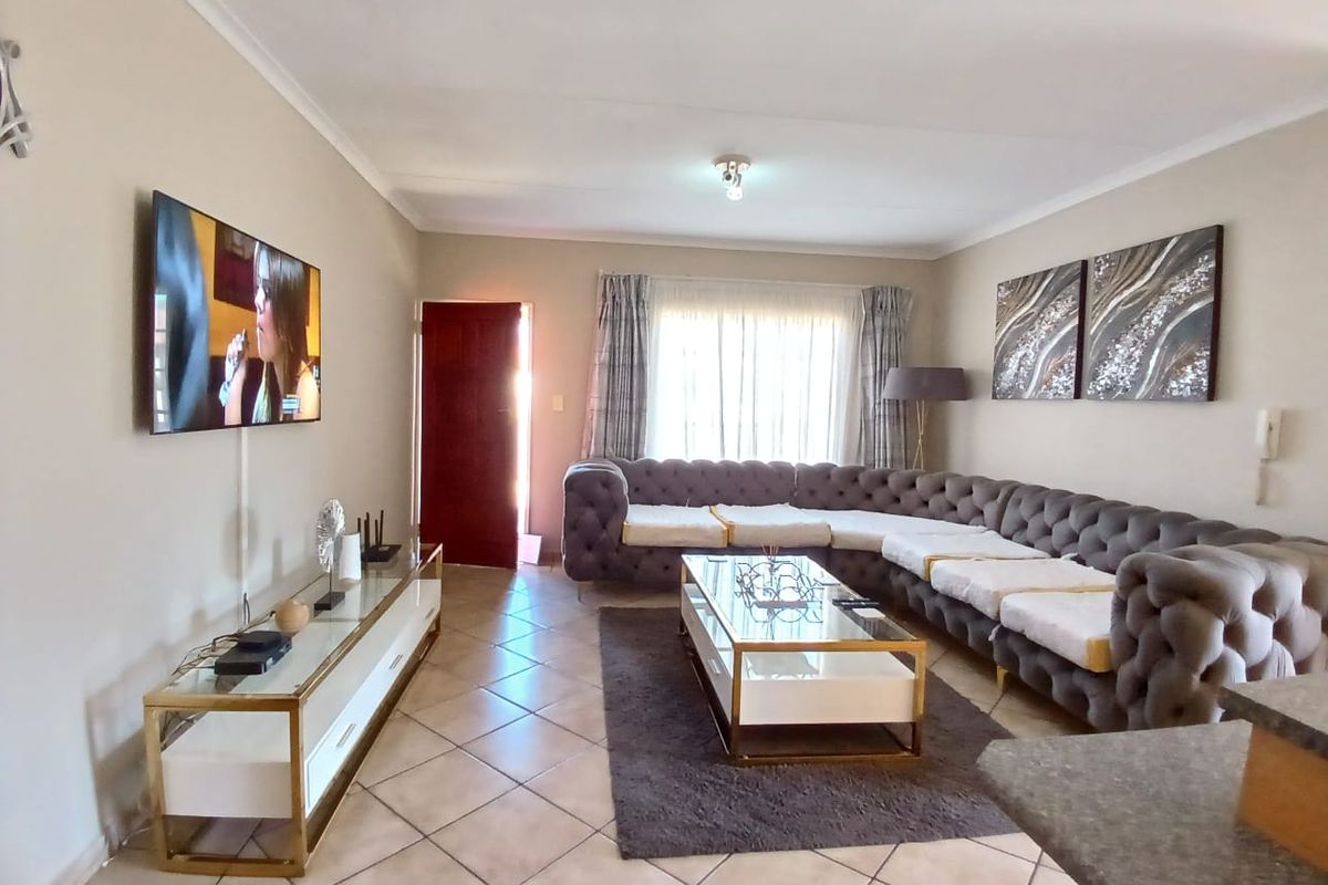 A spacious living room featuring tiled flooring, neutral wall tones, and a large window allowing natural light, creating a comfortable and inviting atmosphere.