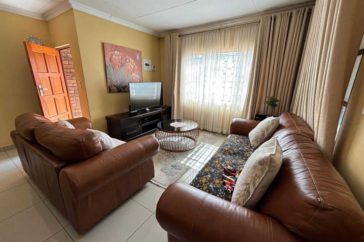 A comfortable living room featuring tiled flooring, crown molding, and large windows with floor-to-ceiling curtains, providing ample natural light.