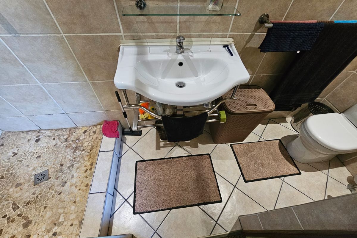 Compact bathroom featuring a wall-mounted basin, tiled shower area with pebble flooring, and standard toilet facilities.