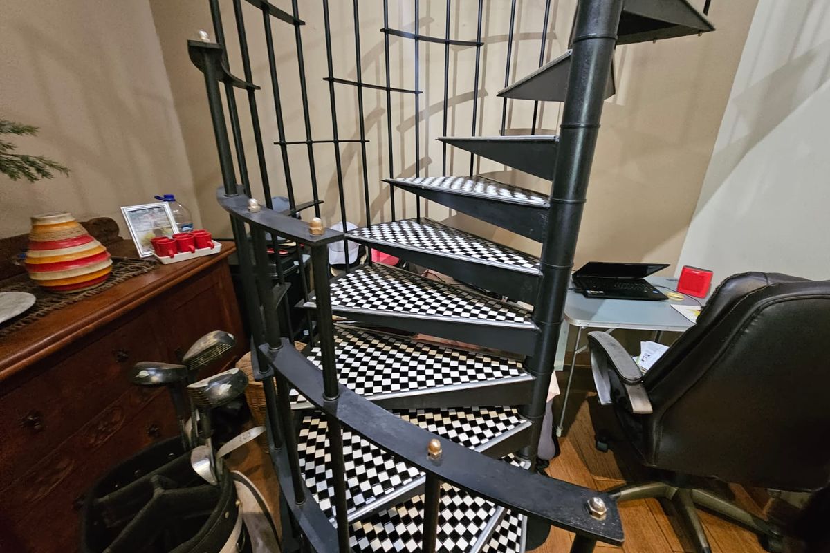 A metal spiral staircase with a distinctive checkered pattern on the treads, serving as a central architectural feature within the living space.