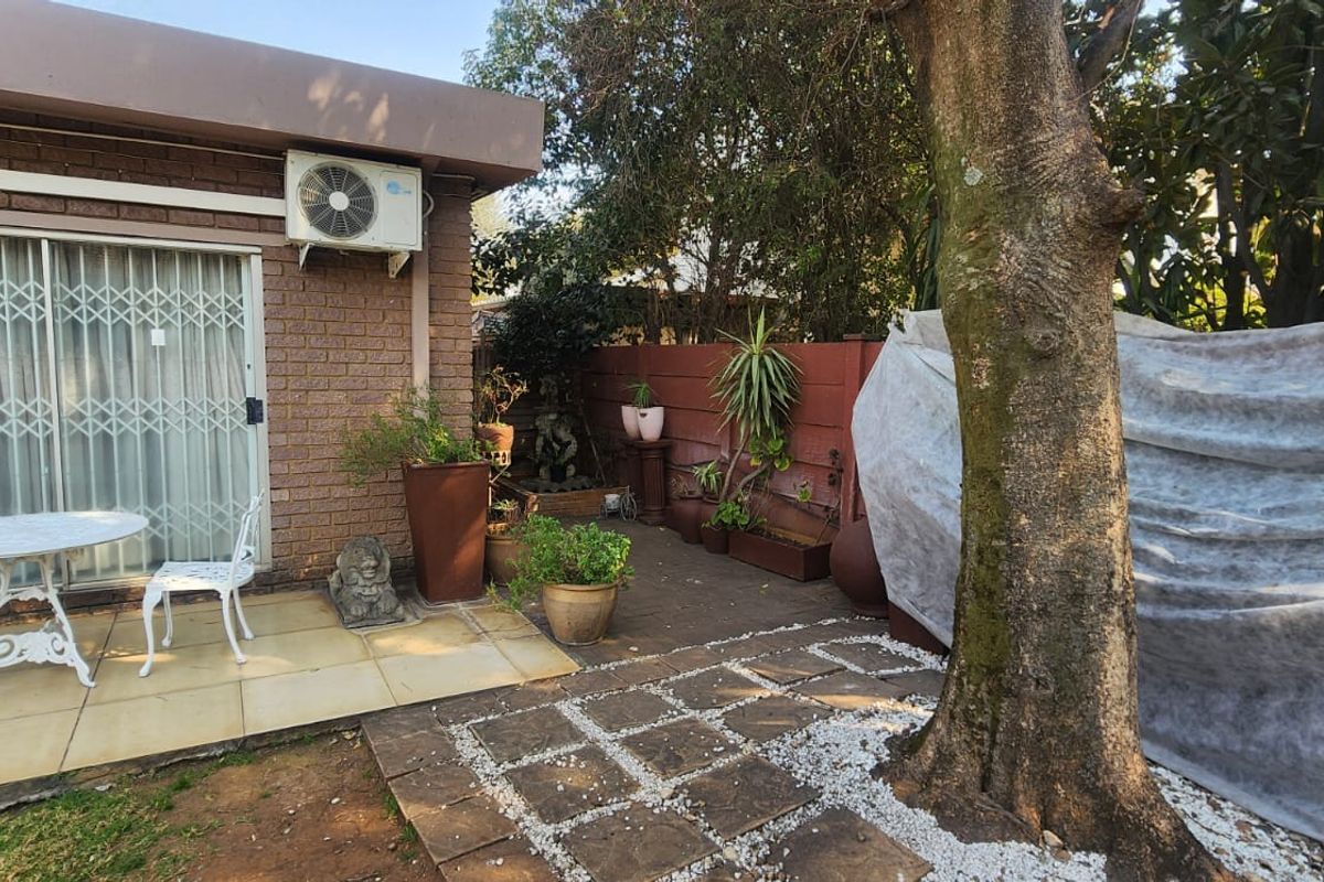 A rear patio area featuring paved flooring, brick exterior walls, and a wall-mounted air conditioning unit, providing a functional outdoor space.