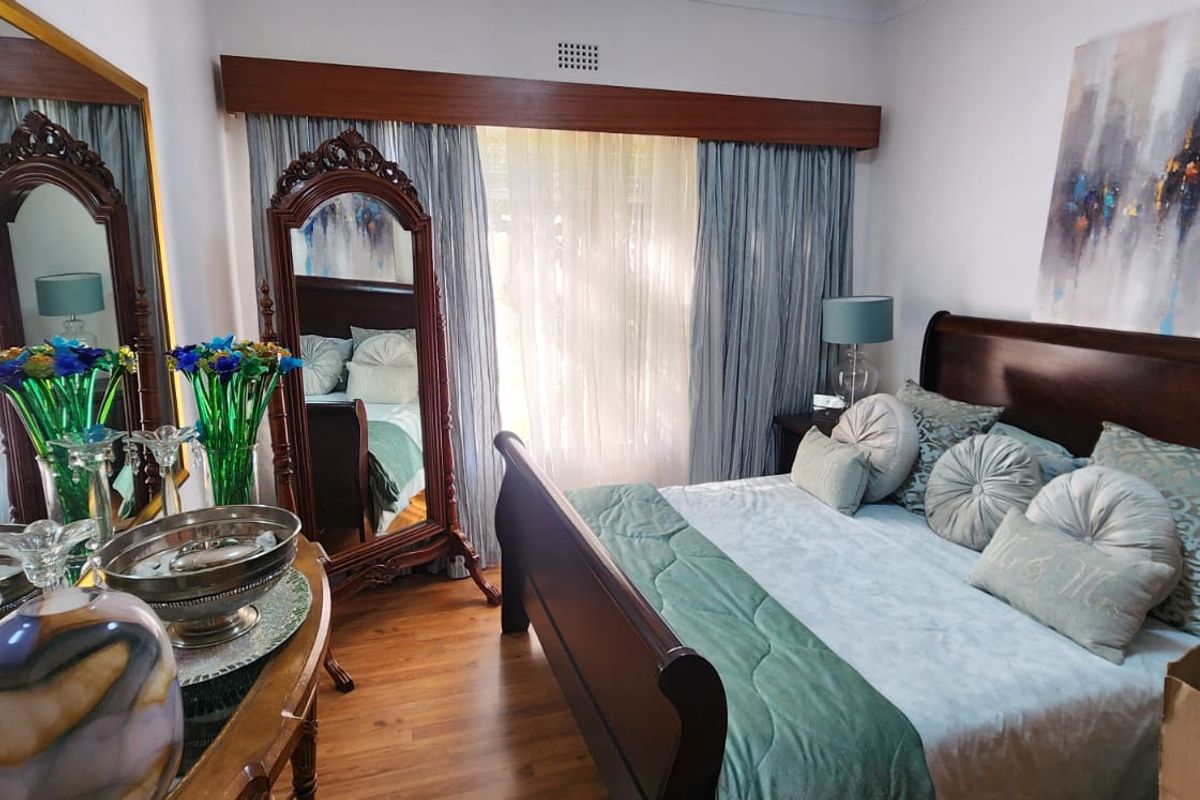 A well-maintained bedroom featuring timber flooring, large windows with curtain pelmets, and ample natural light.