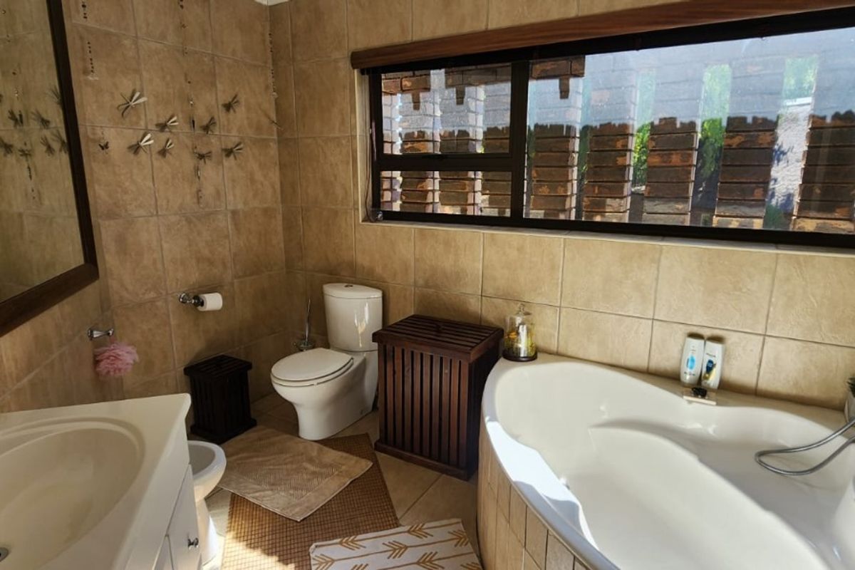 A functional bathroom featuring a corner bathtub, a vanity basin, and a toilet with neutral-toned wall and floor tiling.
