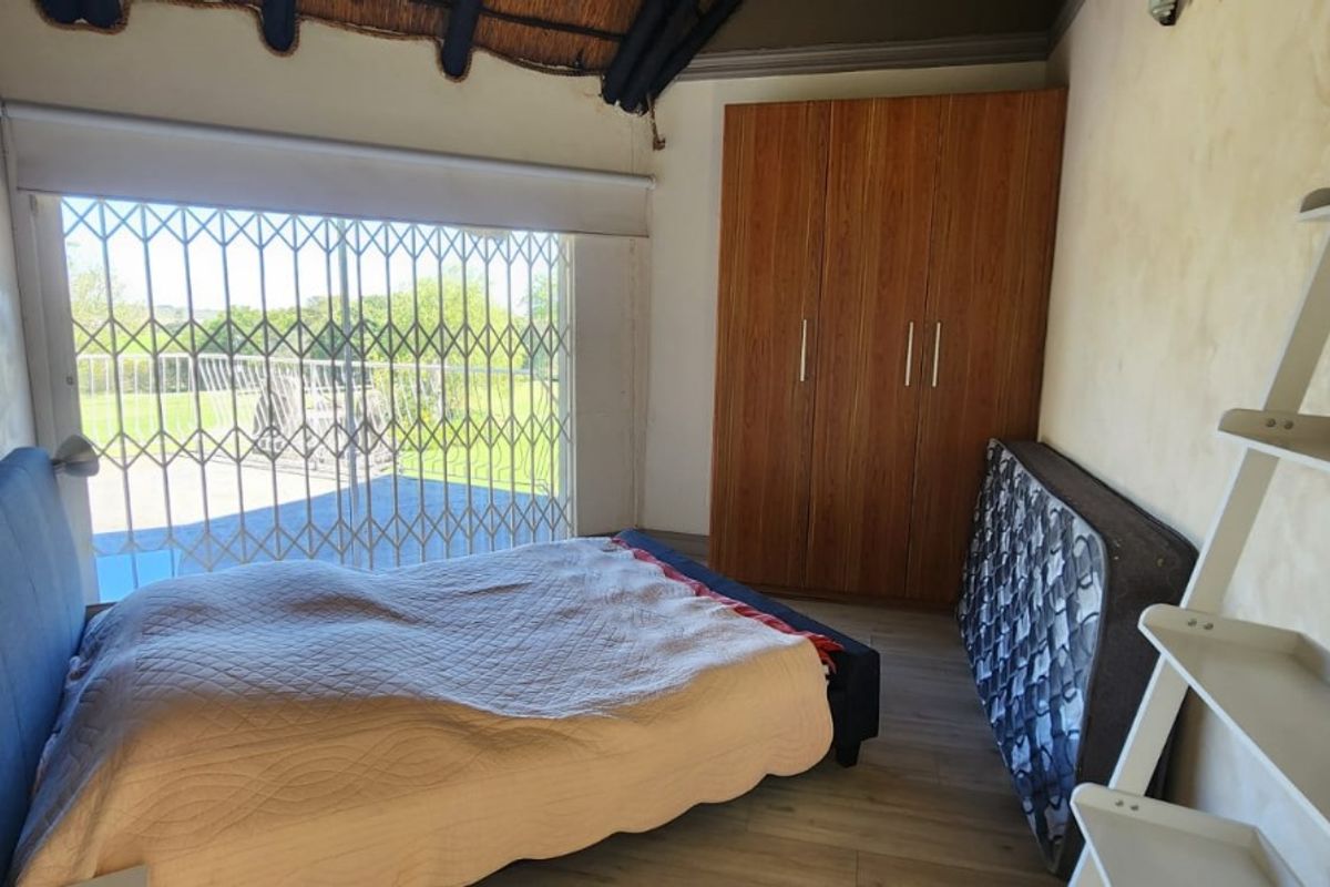A bedroom featuring built-in wooden cupboards, laminate flooring, and a sliding door with security gate leading to an outdoor area.
