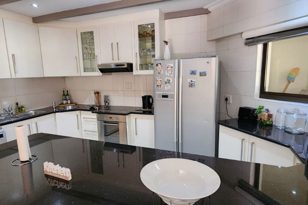 A functional kitchen featuring white cabinetry, black granite countertops, a central island, built-in oven, hob, and extractor fan with tiled splashbacks.