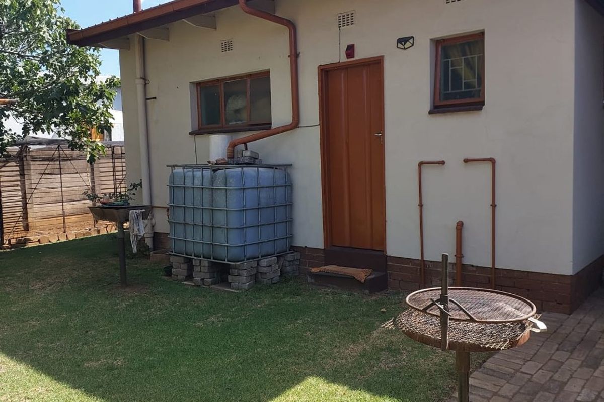 Rear exterior view of the property featuring a lawn, paved area, and external water storage tank with connected guttering system.