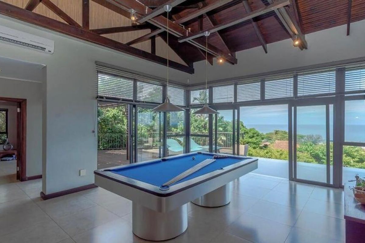 Spacious living area featuring high vaulted timber ceilings, large glass sliding doors opening to a deck, and expansive ocean views.