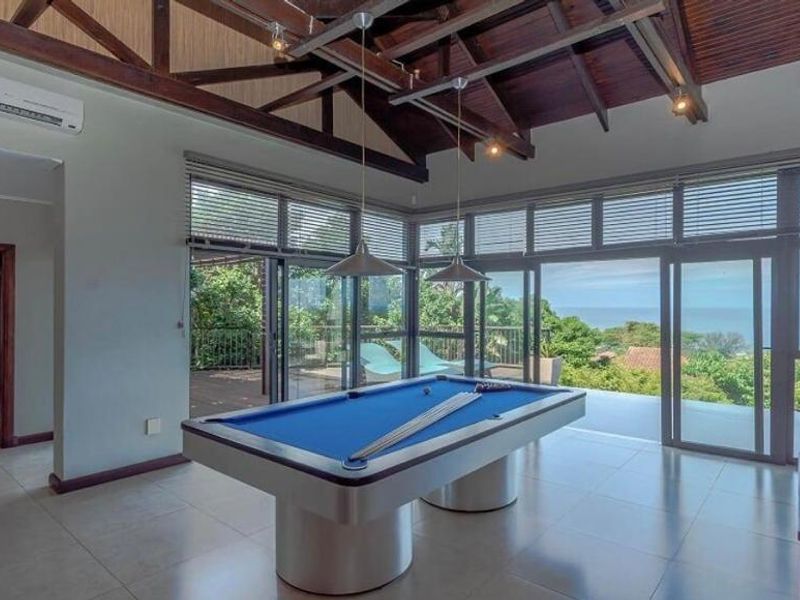 Spacious living area featuring high vaulted timber ceilings, large glass sliding doors opening to a deck, and expansive ocean views.