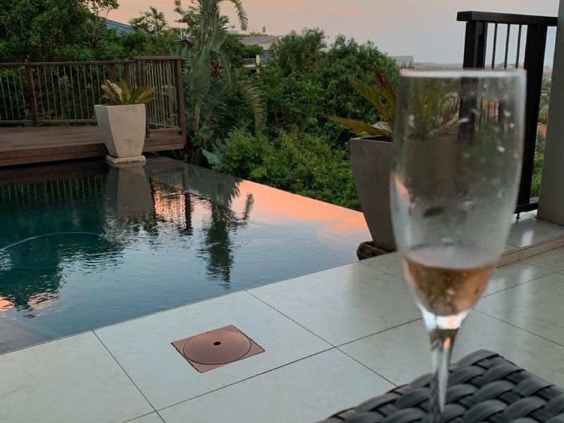 A serene outdoor pool area featuring a modern infinity-edge pool, tiled patio, and elevated wooden decking, set against a scenic sunset backdrop.