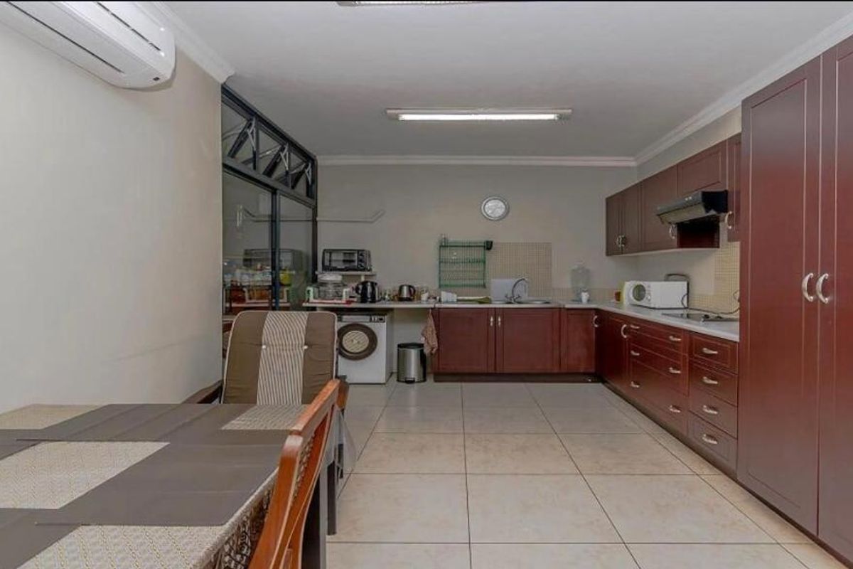 A functional kitchen featuring dark wood cabinetry, tiled flooring, a built-in hob, and an integrated extractor fan, with an adjacent dining area.