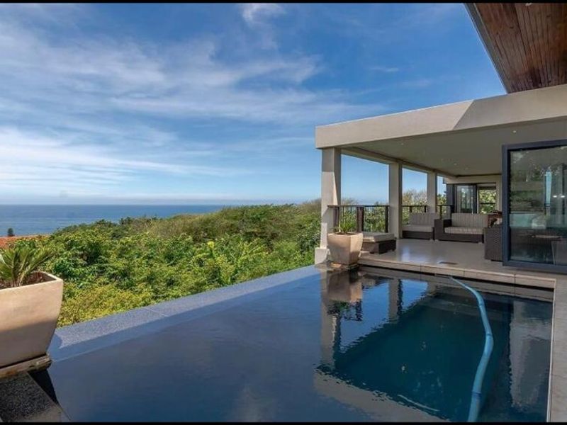 A stunning infinity-edge swimming pool overlooking the ocean, featuring a covered patio area with seamless indoor-outdoor flow.