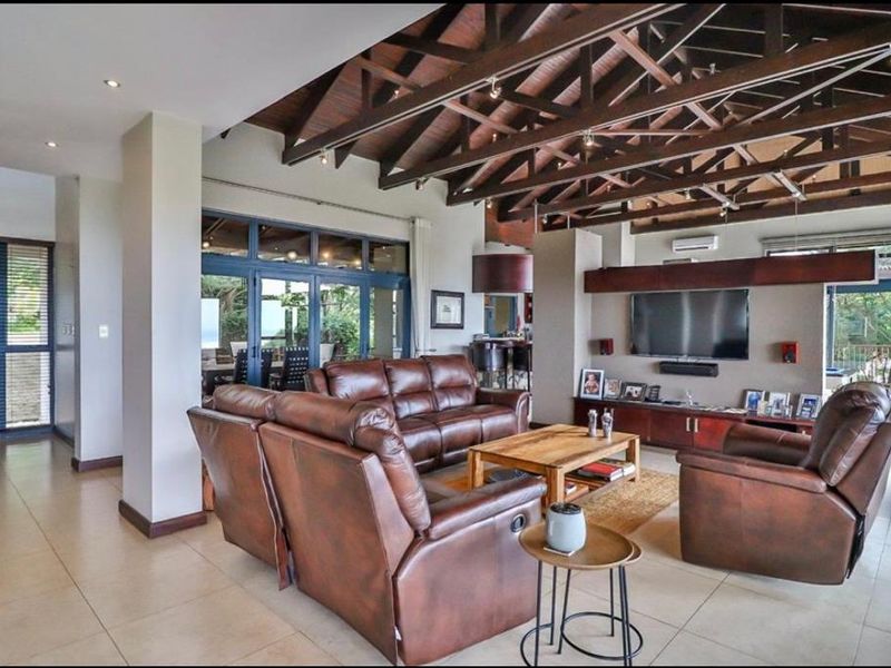 Spacious open-plan living area featuring high vaulted timber beam ceilings, tiled flooring, and large glass sliding doors leading to an outdoor patio.