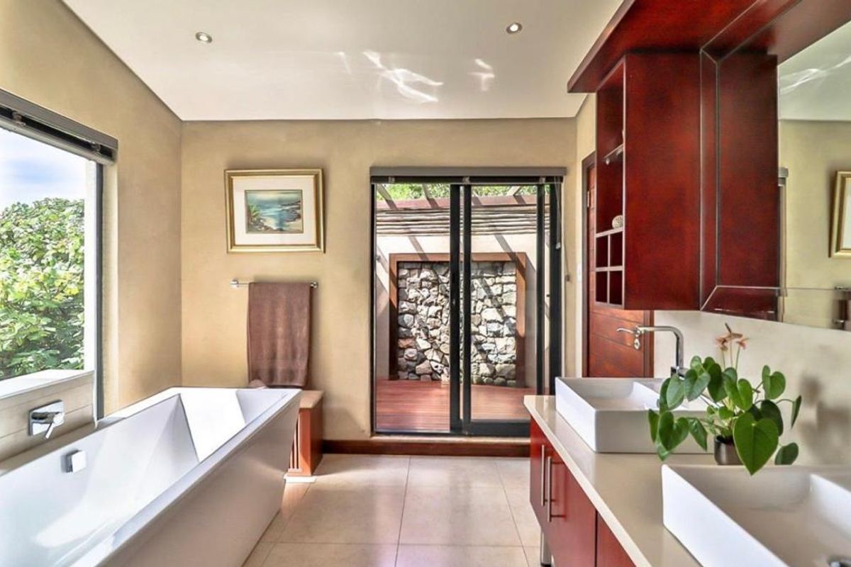 A modern bathroom featuring a freestanding bathtub, dual vessel sinks on a wooden vanity, and sliding glass doors opening to a private outdoor area.