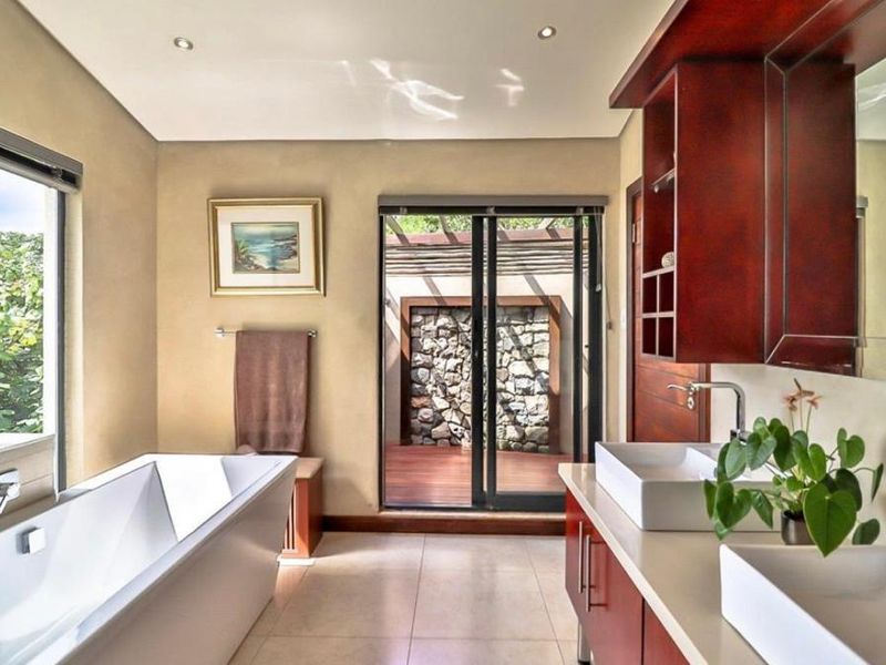 A modern bathroom featuring a freestanding bathtub, dual vessel sinks on a wooden vanity, and sliding glass doors opening to a private outdoor area.