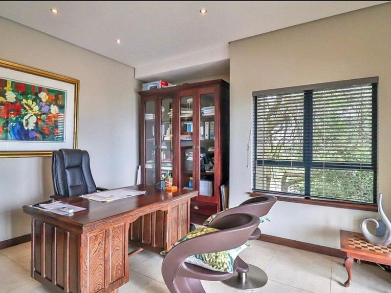 A well-lit home office featuring tiled flooring, recessed ceiling lighting, and a large window with fitted blinds.