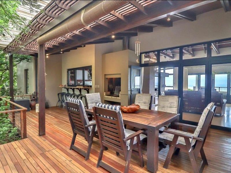 Spacious covered timber deck featuring a built-in braai, exposed beam ceiling, and direct access to the interior living area through large glass doors.