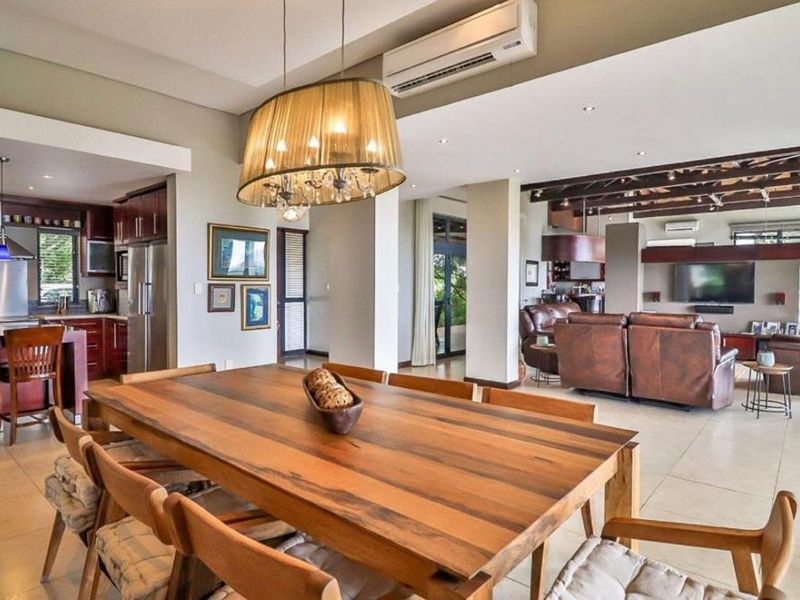 Spacious open-plan living and dining area featuring tiled flooring, recessed lighting, and a modern kitchen with dark wood cabinetry and stainless steel appliances.