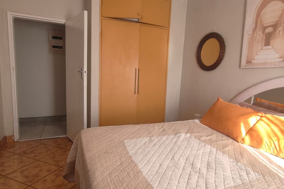 A bedroom featuring built-in cupboards, tiled flooring, and a doorway leading to an adjacent space.