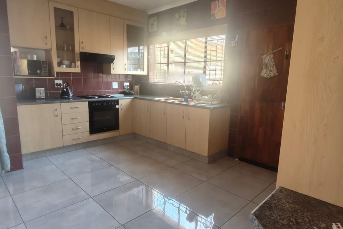 A functional kitchen featuring light wood cabinetry, dark tiled splashbacks, a built-in oven and hob, and large format floor tiles.