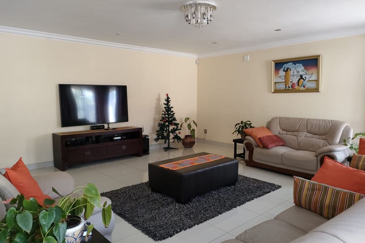 A spacious, well-maintained living room featuring neutral tiled flooring, decorative cove cornicing, and a central crystal chandelier, providing a bright and comfortable living space.