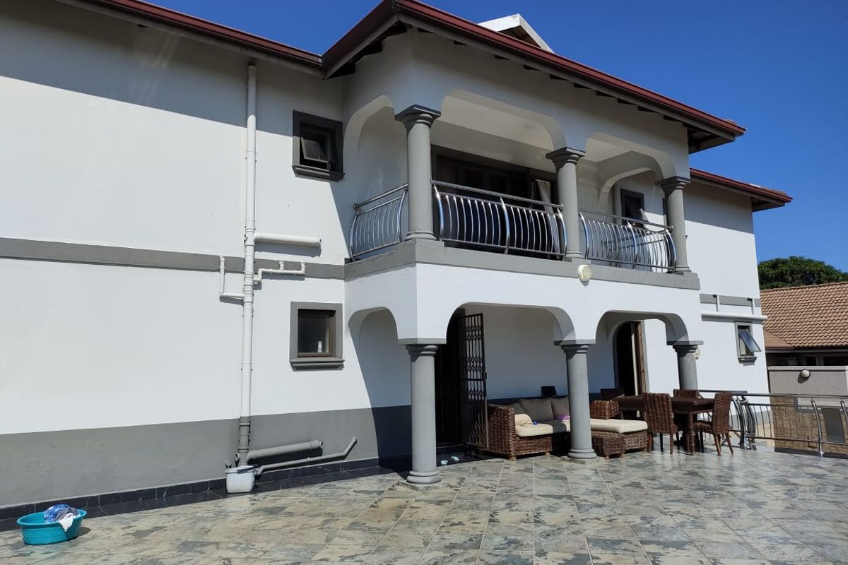Rear elevation featuring a spacious tiled patio, a covered balcony with stainless steel balustrades, and classic architectural columns.