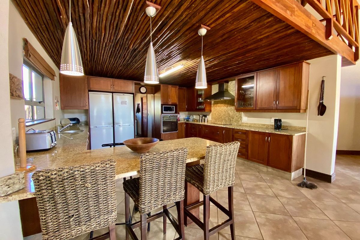 Spacious kitchen featuring wooden cabinetry, granite countertops, a breakfast island, and a unique rustic timber-slat ceiling with a mezzanine level above.