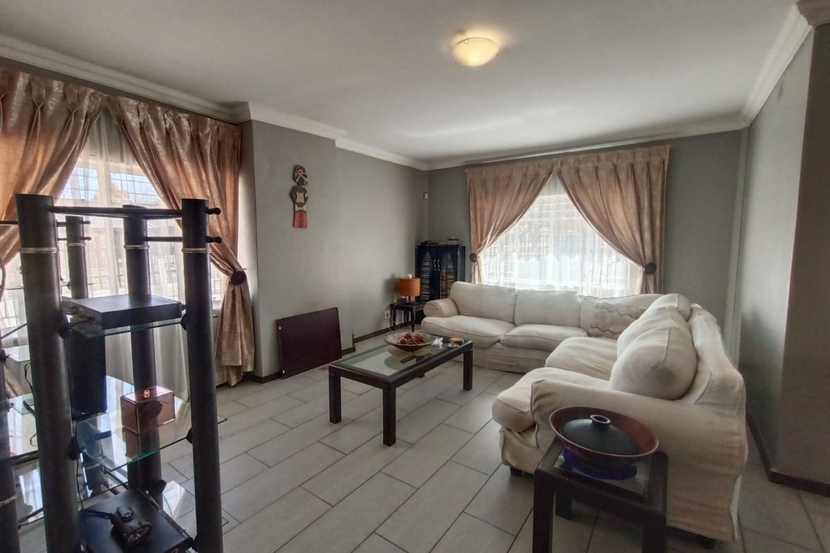 A spacious living room featuring neutral grey walls, tiled flooring, and decorative ceiling cornices, providing a comfortable and functional living space.