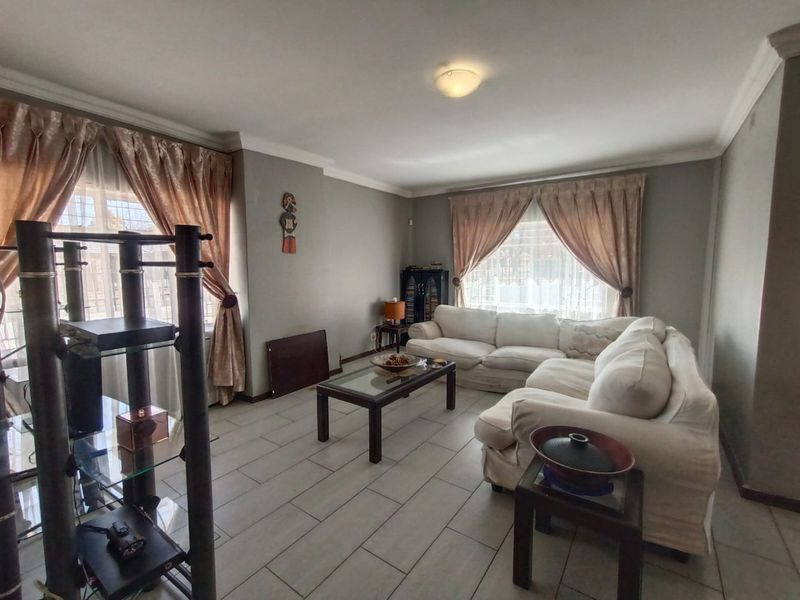 A spacious living room featuring neutral grey walls, tiled flooring, and decorative ceiling cornices, providing a comfortable and functional living space.