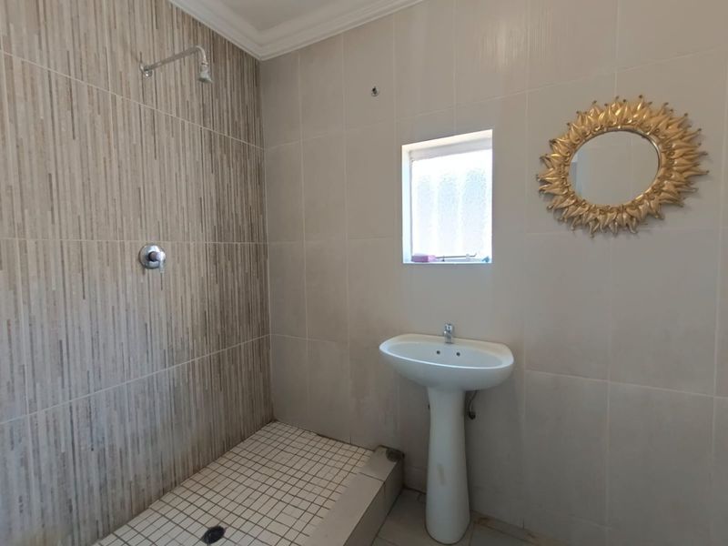 A functional bathroom featuring a pedestal basin, tiled shower area with wall-mounted shower head, and neutral wall tiling.