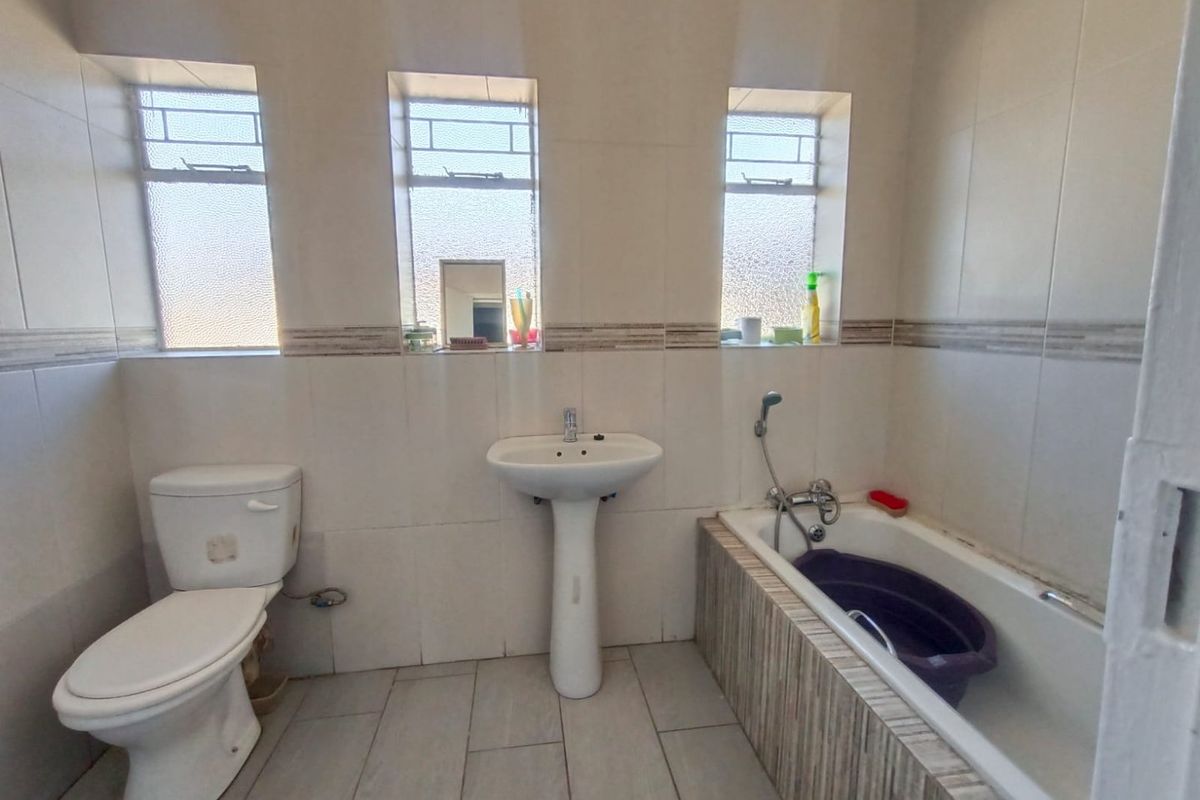 A functional bathroom featuring a pedestal basin, toilet, and bathtub with tiled finishes and three windows providing natural light.