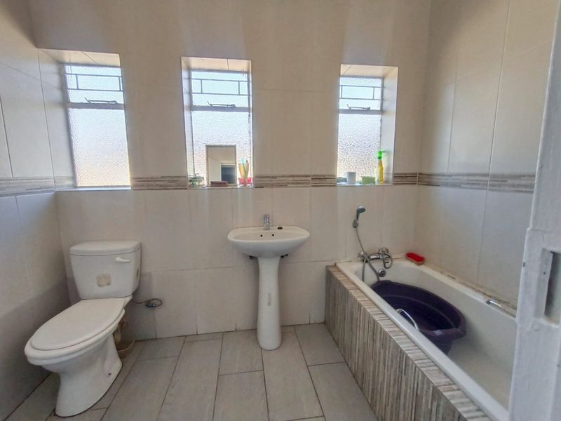 A functional bathroom featuring a pedestal basin, toilet, and bathtub with tiled finishes and three windows providing natural light.