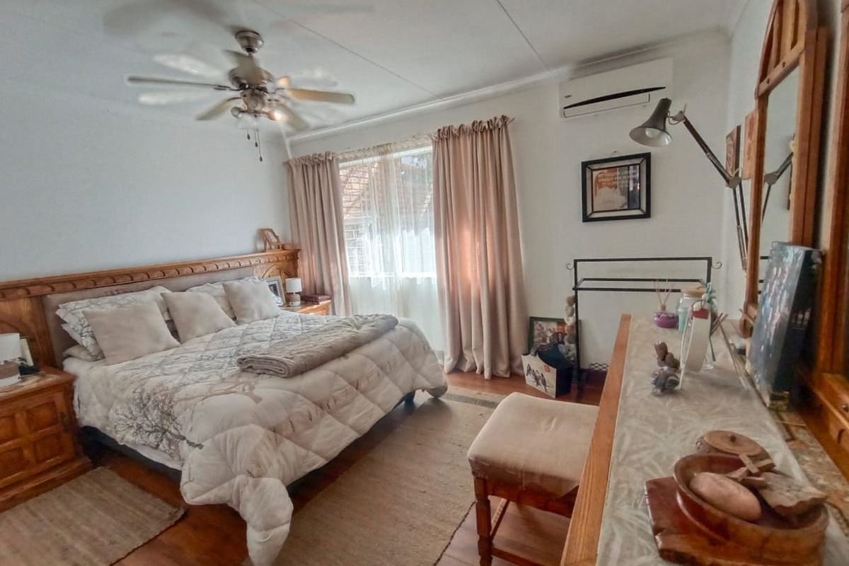 A well-maintained bedroom featuring a ceiling fan, wall-mounted air conditioning unit, and timber flooring.