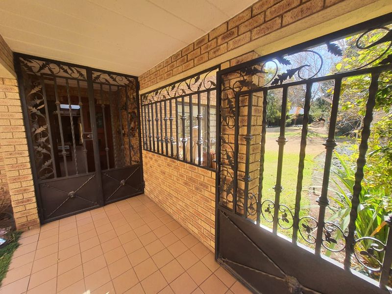 A covered patio area featuring face brick walls, tiled flooring, and decorative wrought iron security gates and window bars overlooking the garden.