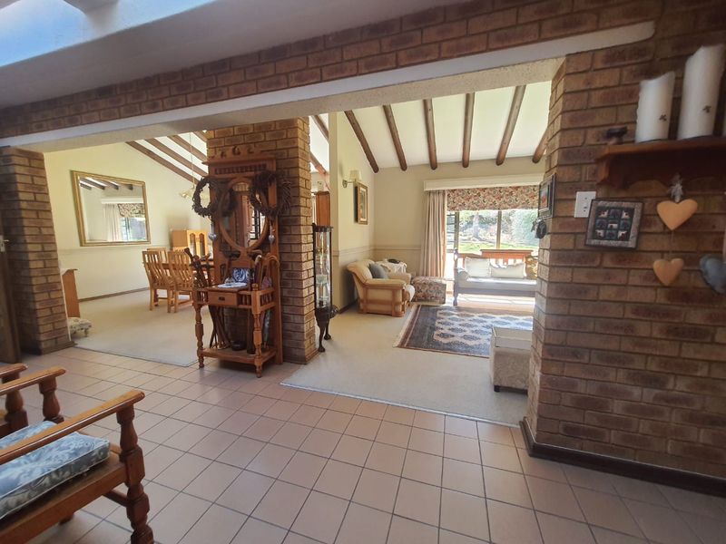 Spacious open-plan living and dining area featuring exposed timber ceiling beams, facebrick walls, and large sliding doors leading to the garden.