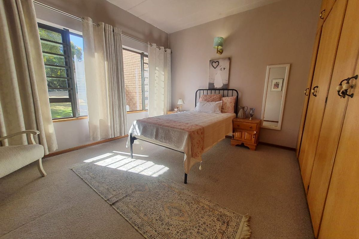 A well-lit bedroom featuring built-in wooden cupboards, neutral carpeting, and large windows that provide ample natural light.