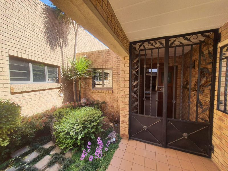 A covered entrance area featuring face brick walls, a decorative wrought iron security gate, and tiled flooring leading to a timber front door.