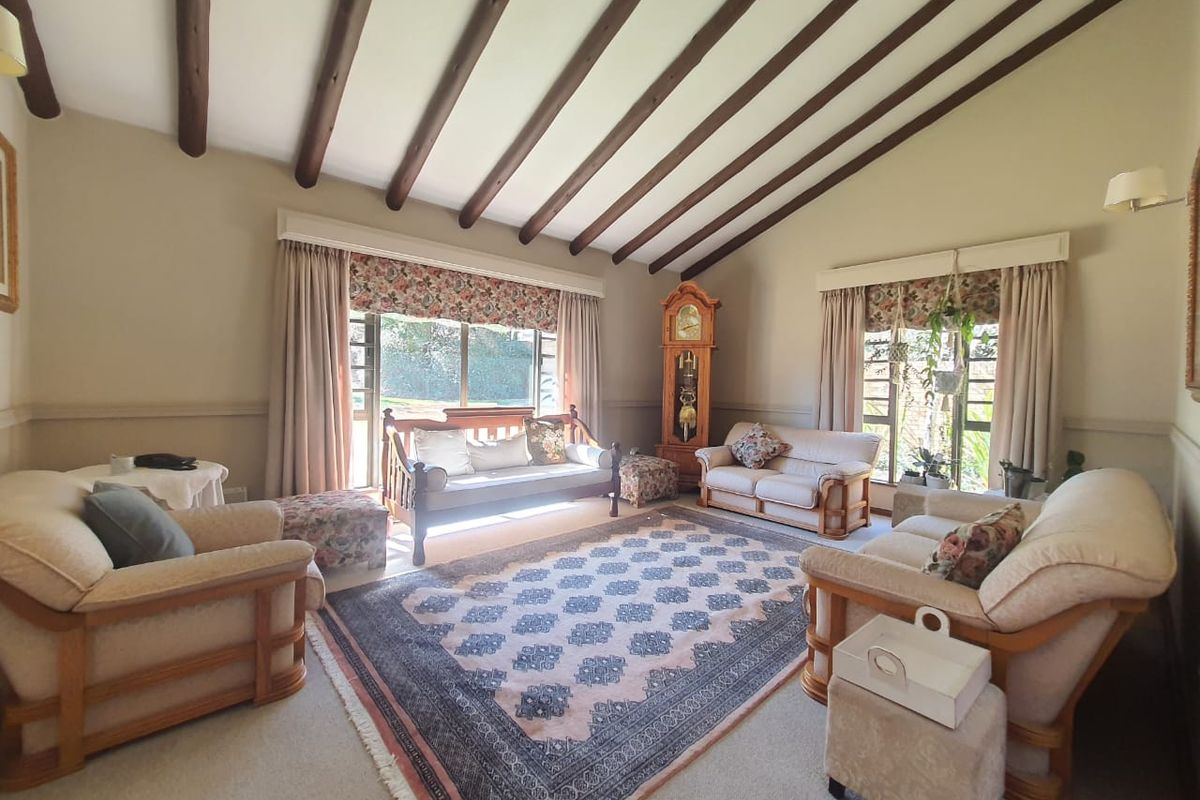 Spacious living room featuring a vaulted ceiling with exposed timber beams, large windows providing natural light, and a classic dado rail finish.