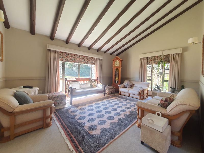 Spacious living room featuring a vaulted ceiling with exposed timber beams, large windows providing natural light, and a classic dado rail finish.